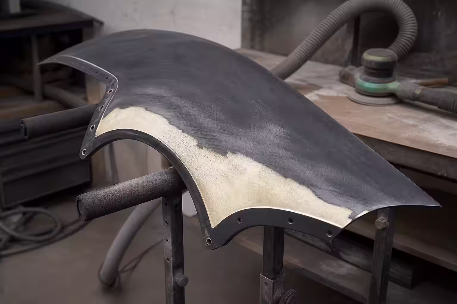 Detalle de un guardafango de fibra de vidrio sobre una mesa de trabajo con herramientas al fondo.